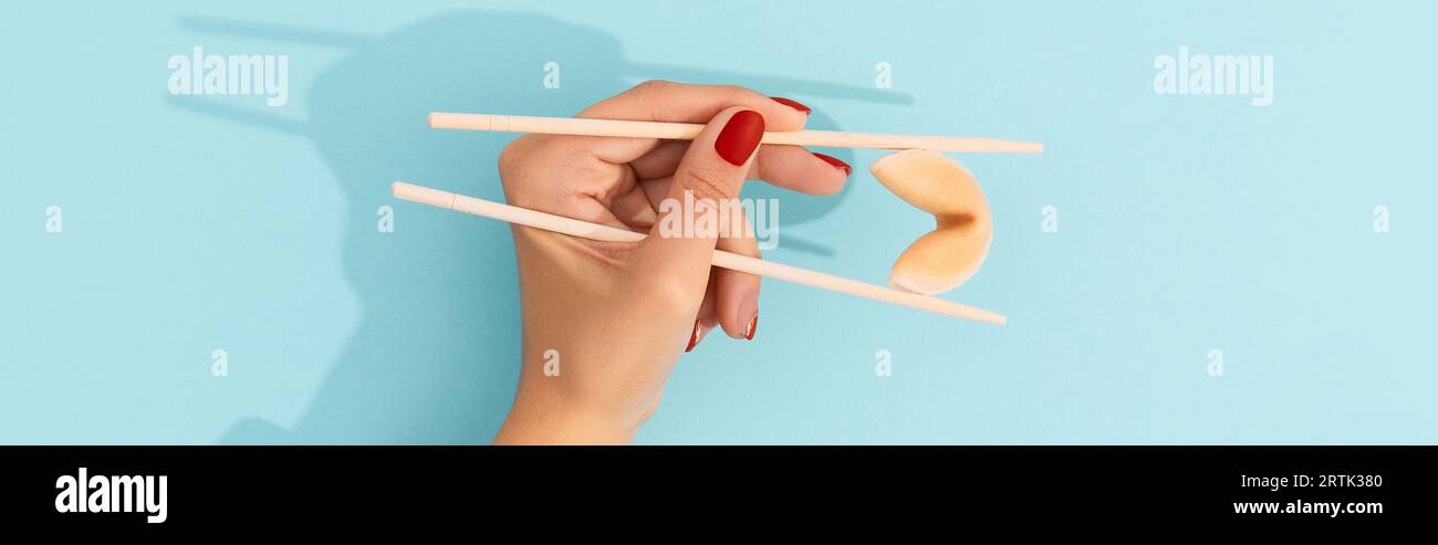 Biscotti di fortuna di tenuta della mano femminile con i chopsticks cinesi su sfondo blu Foto Stock