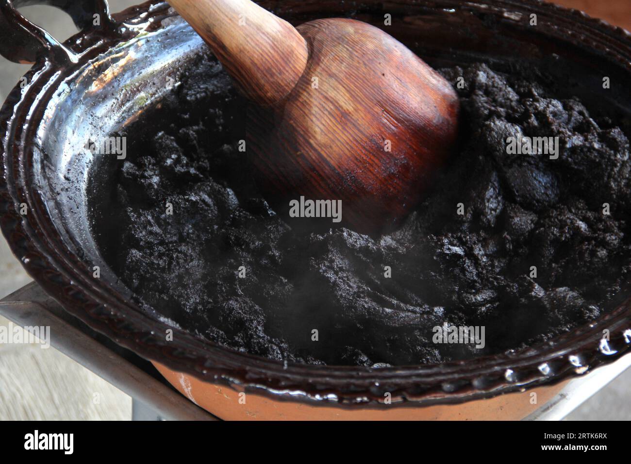 Preparazione della talpa rossa, un tipico piatto messicano in una pentola di argilla con un gigantesco cucchiaio di legno sul fuoco di una stufa con tutti gli ingredienti integrati Foto Stock