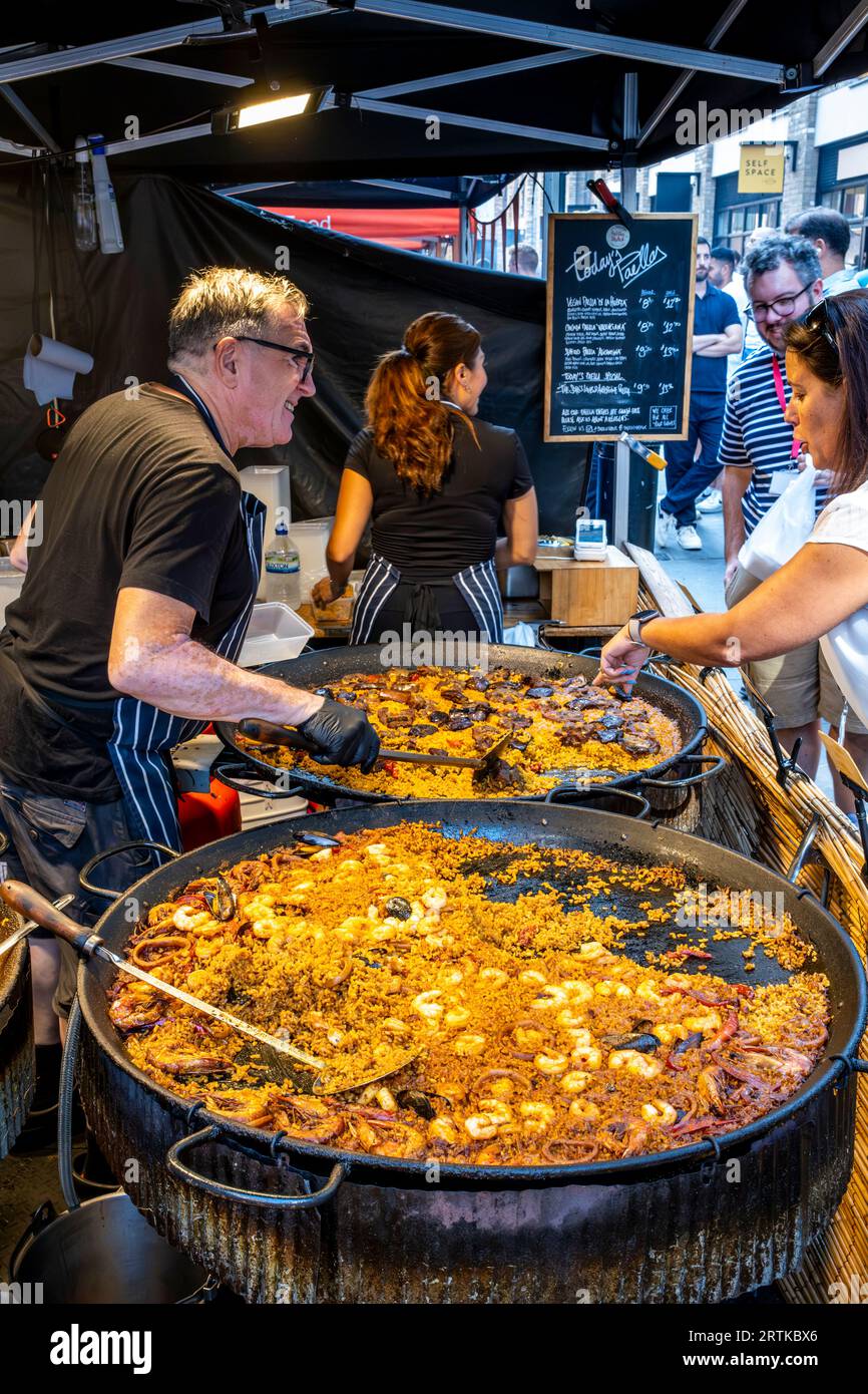 A Man serve paella presso Uno Street Food Stall, Berwick Street, Londra, Regno Unito. Foto Stock