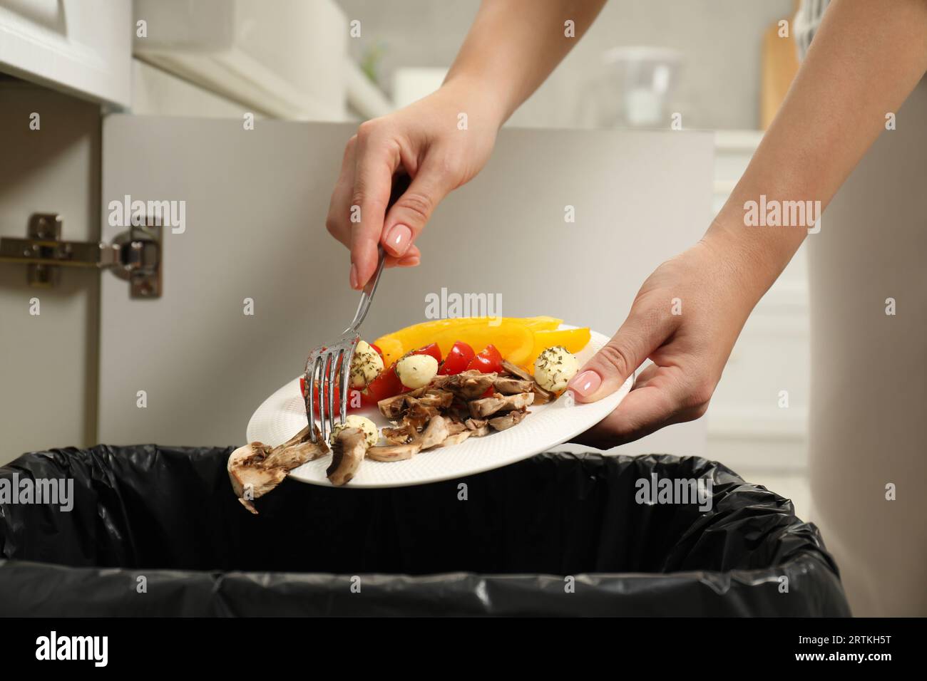 Donna che lancia verdure e funghi nel bidone in casa, primo piano Foto Stock