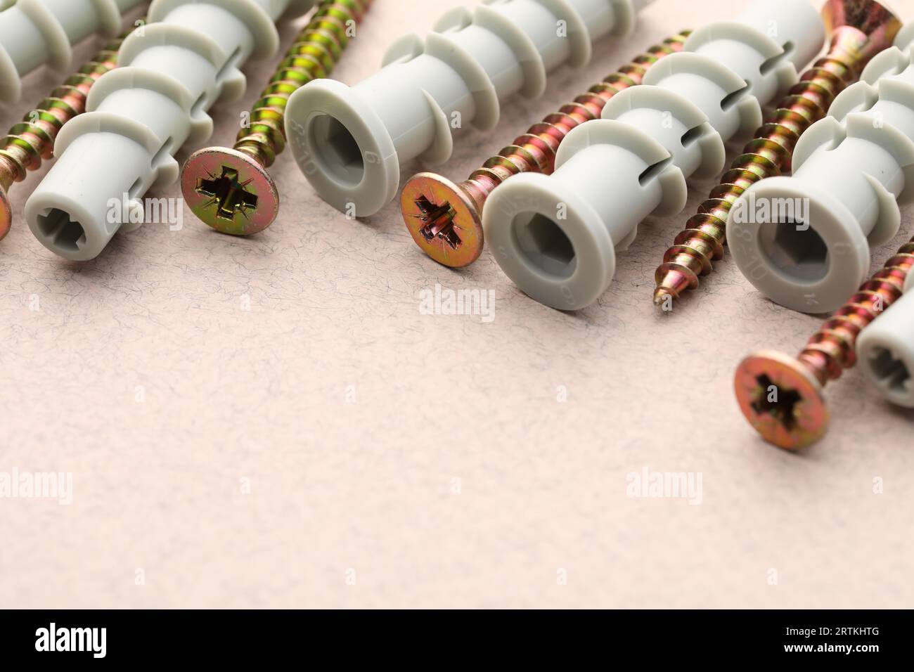 Molte viti e tasselli metallici su un tavolo ruvido beige, primo piano. Spazio per il testo Foto Stock