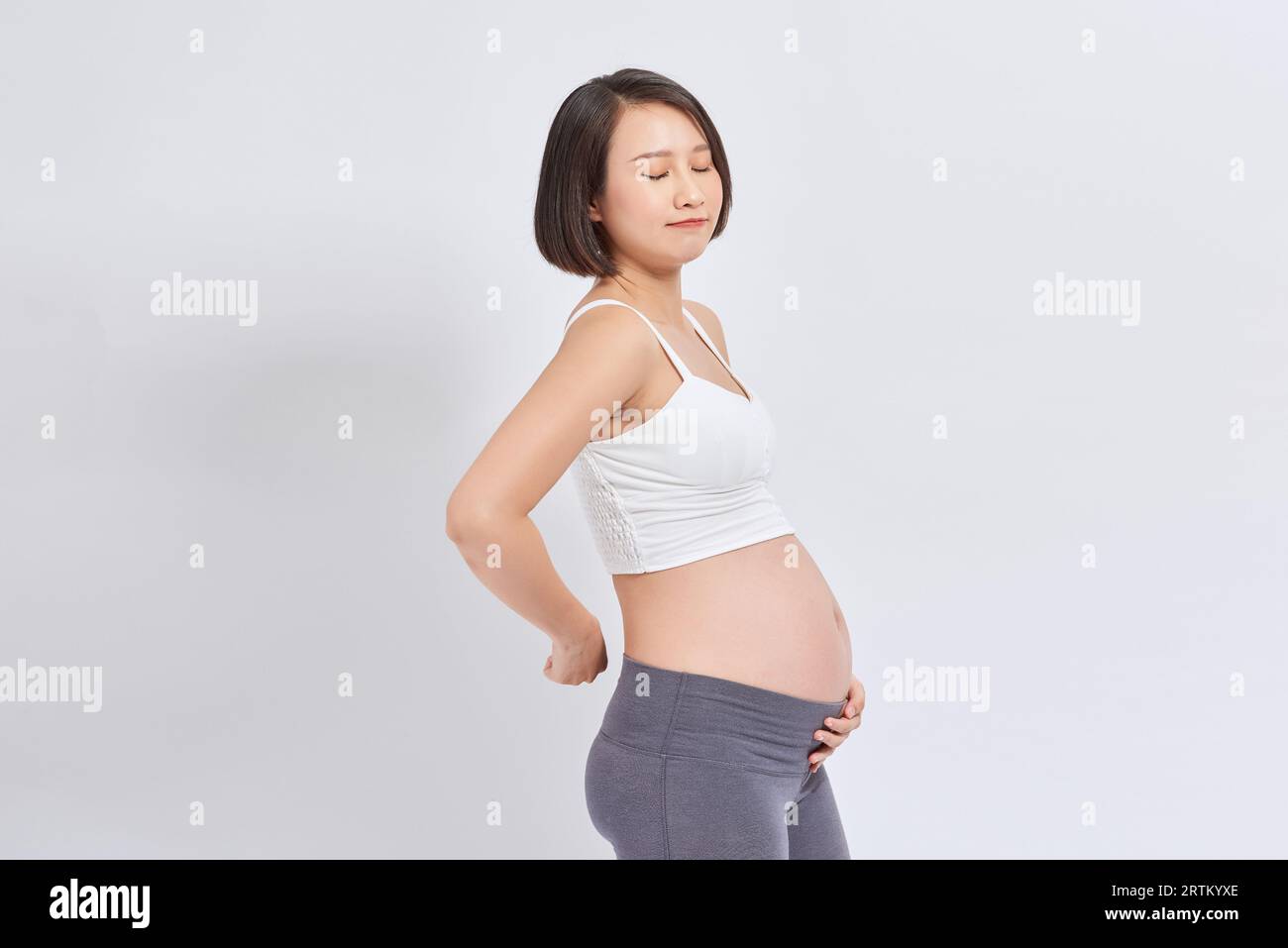 Giovane bella donna asiatica incinta in piedi e toccare pancia e schiena Foto Stock