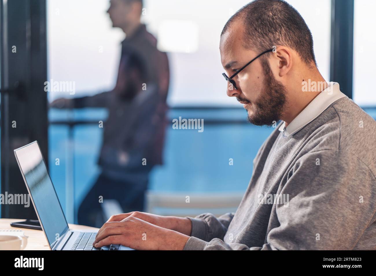 Giovane uomo d'affari che lavora su un notebook in ufficio. Ritratto del tecnico del software IT in occhiali, vista laterale. Foto Stock