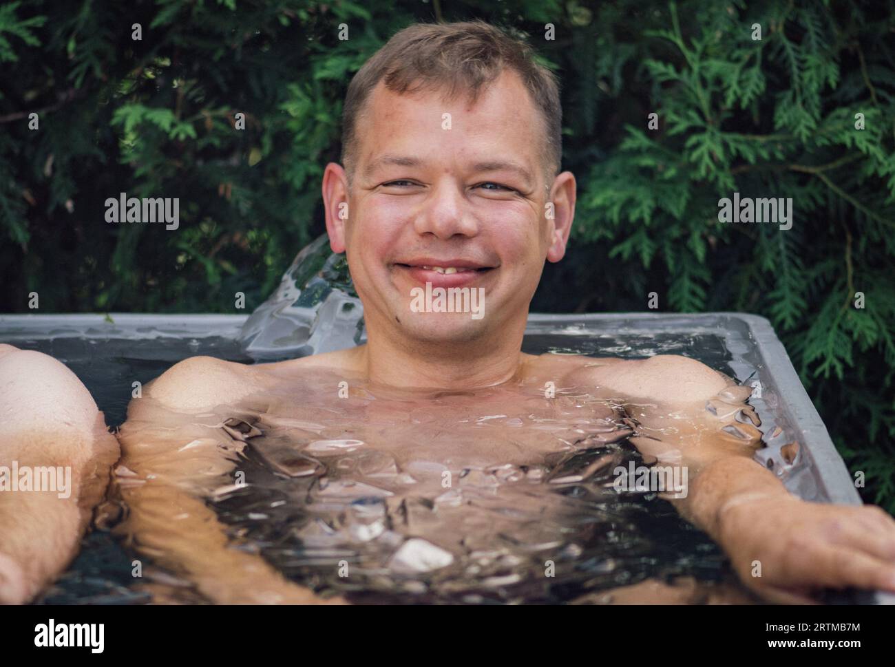 L'uomo fa il bagno di ghiaccio nell'acqua fredda tra i cubetti di ghiaccio. Metodo Wim Hof, terapia fredda, tecniche respiratorie, yoga e meditazione Foto Stock