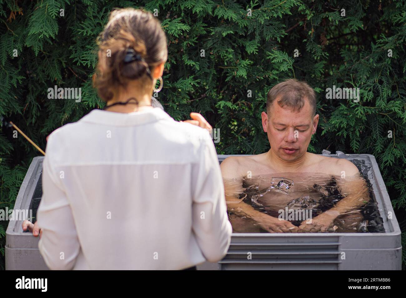 Uomo che fa il bagno di ghiaccio nell'acqua fredda tra cubetti di ghiaccio con istruttore. Metodo Wim Hof, terapia fredda, tecniche respiratorie, yoga e meditazione Foto Stock