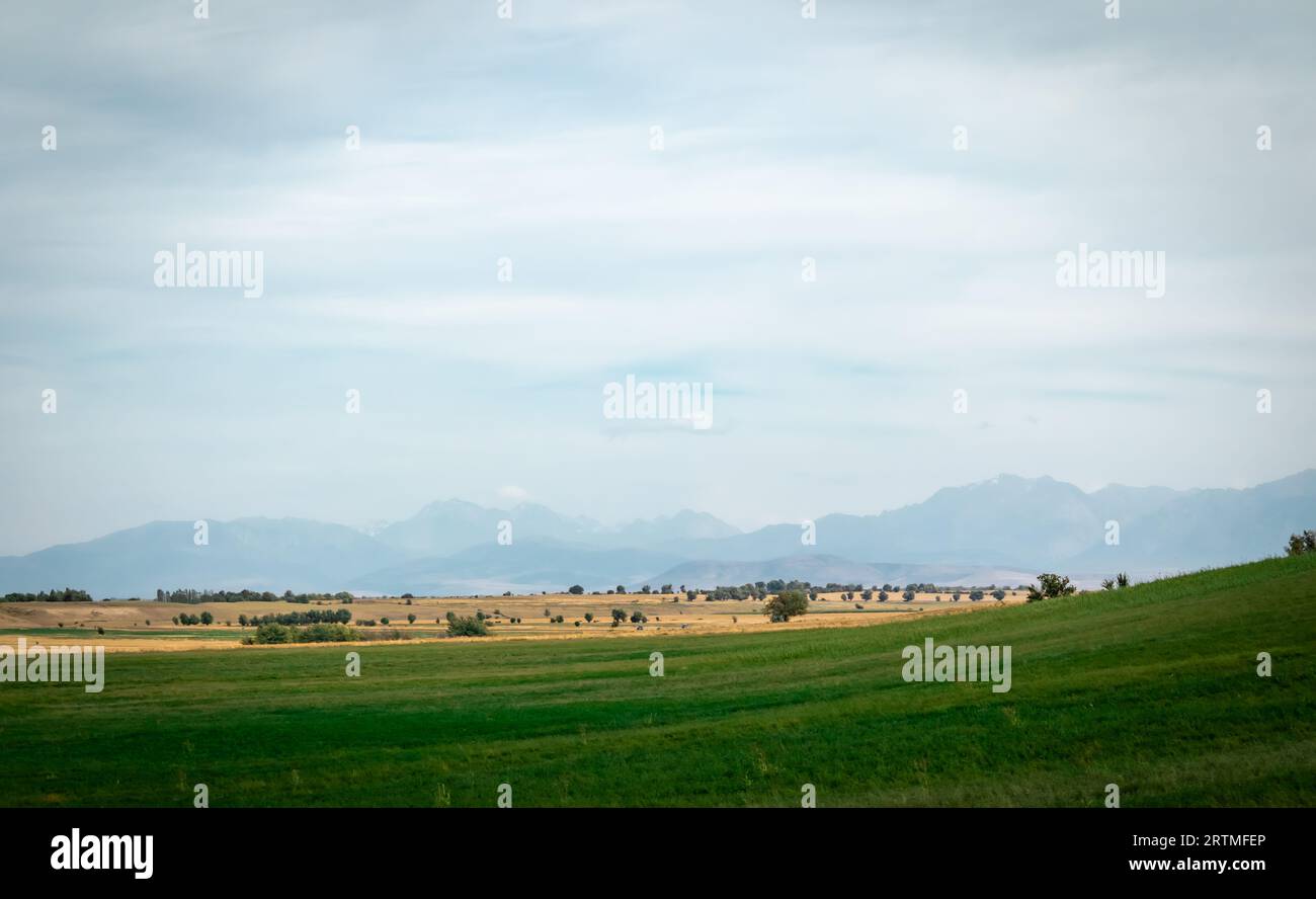 verde collina sullo sfondo di alte montagne e nuvole di tempeste Foto Stock