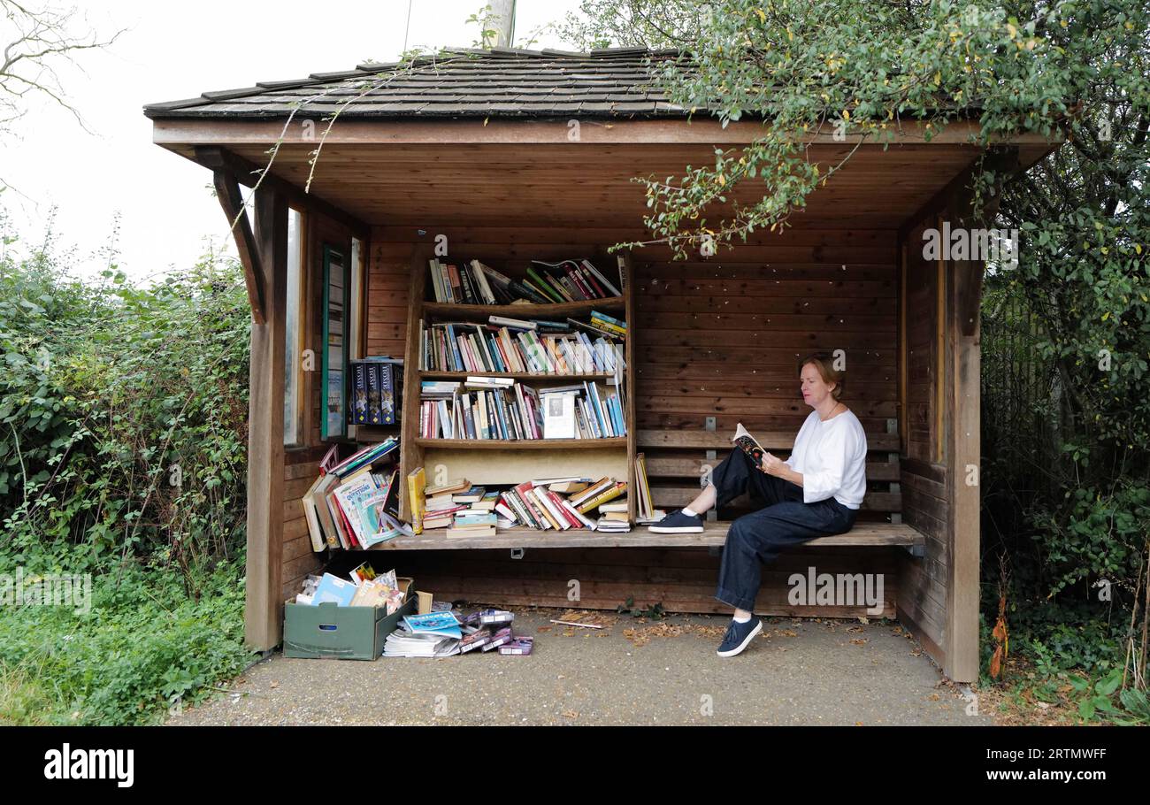 Una donna che aspetta un autobus mentre legge un libro in una fermata piena di vecchi libri Foto Stock