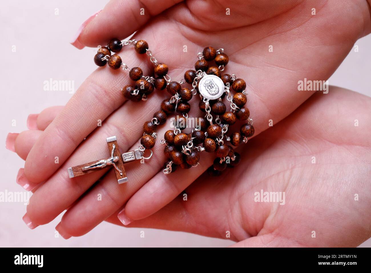 Le mani di una donna che tiene il rosario cattolico di legno in preghiera. Foto Stock