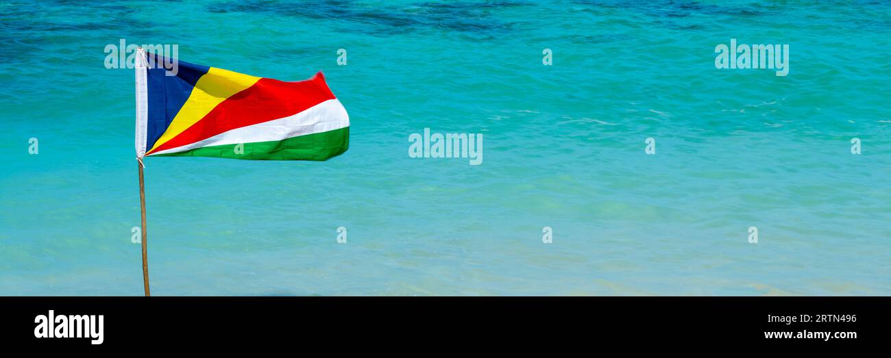 Bandiera delle Seychelles su una spiaggia, sfondo panoramico d'acqua turchese con spazio copia, banner web di viaggio delle Seychelles Foto Stock