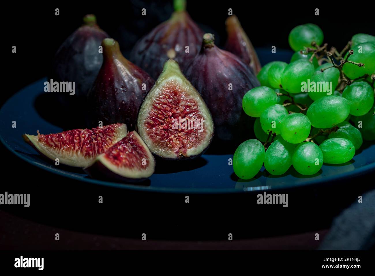 Fichi biologici con uva su un piatto su sfondo nero, primo piano, fotografia macro Foto Stock