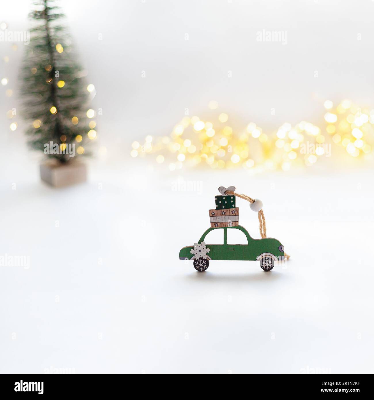 Auto verde in legno con regali di Capodanno sul tetto su sfondo bianco. Albero di Natale e luci bokeh sullo sfondo trasporti e logisti Foto Stock