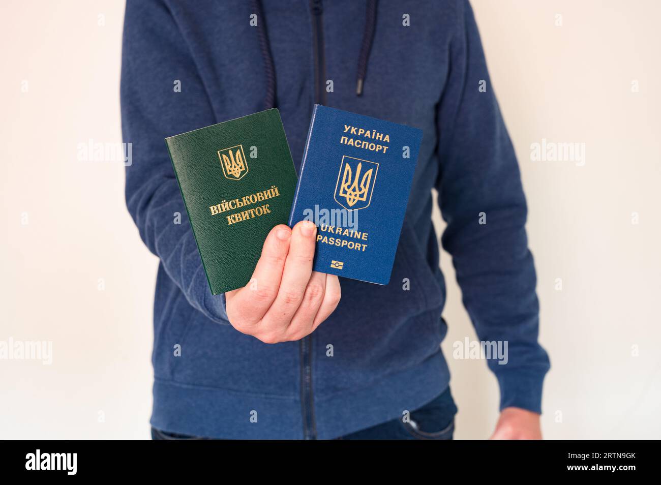 Traduzione: "id militare". Uomo civile in felpa blu con passaporto ucraino straniero e documento militare per soldati, principianti e civili in mano Foto Stock
