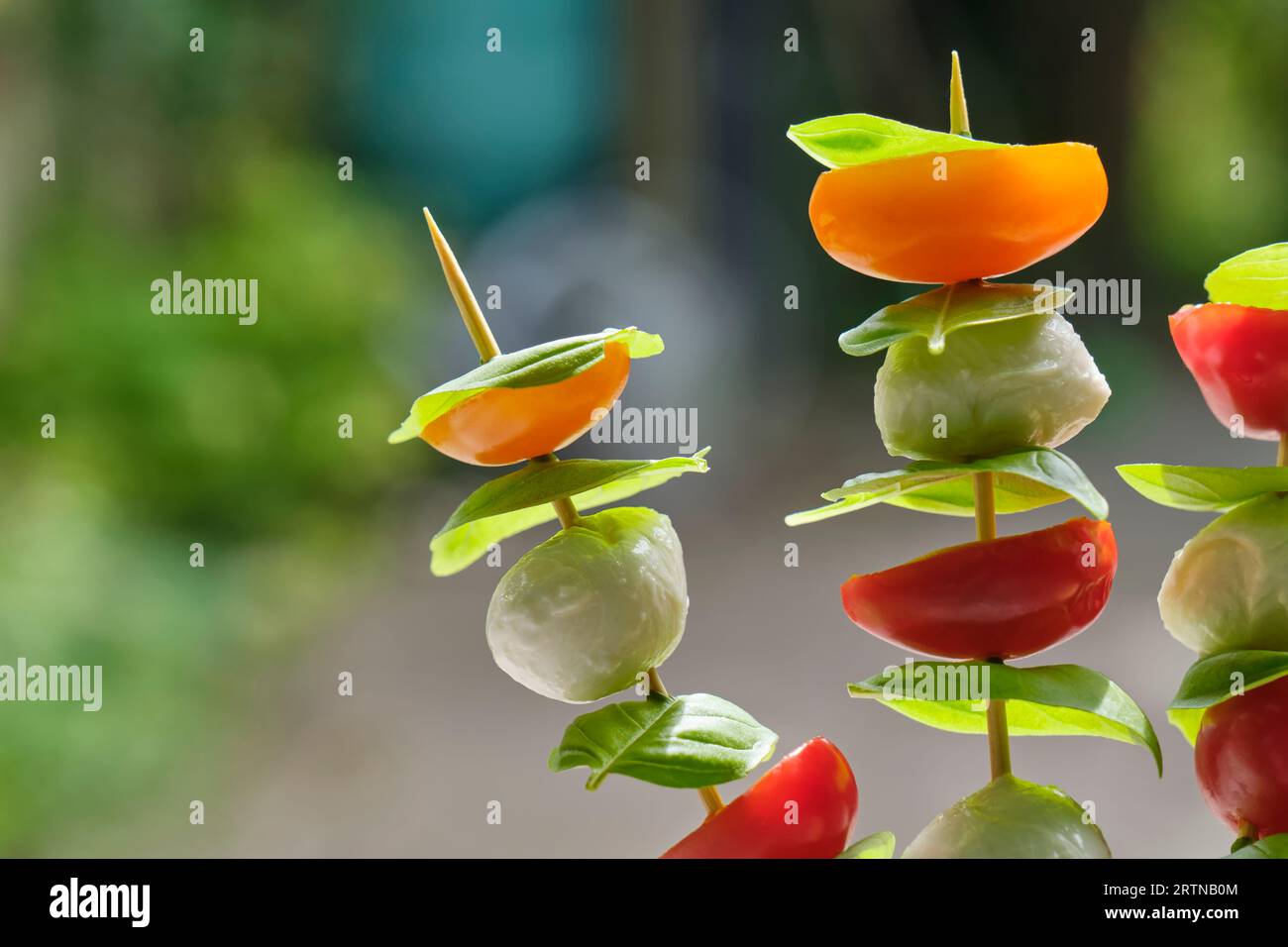 Sano spuntino estivo su spiedini con pomodoro rosso e arancia, basilico e formaggio di capra. Immagine con messa a fuoco selettiva e spazio di copia. Foto Stock