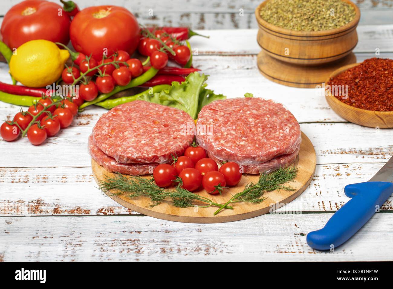 Polpettine di hamburger crude su sfondo di legno. Hamburger crudo di vitello con erbe e spezie Foto Stock