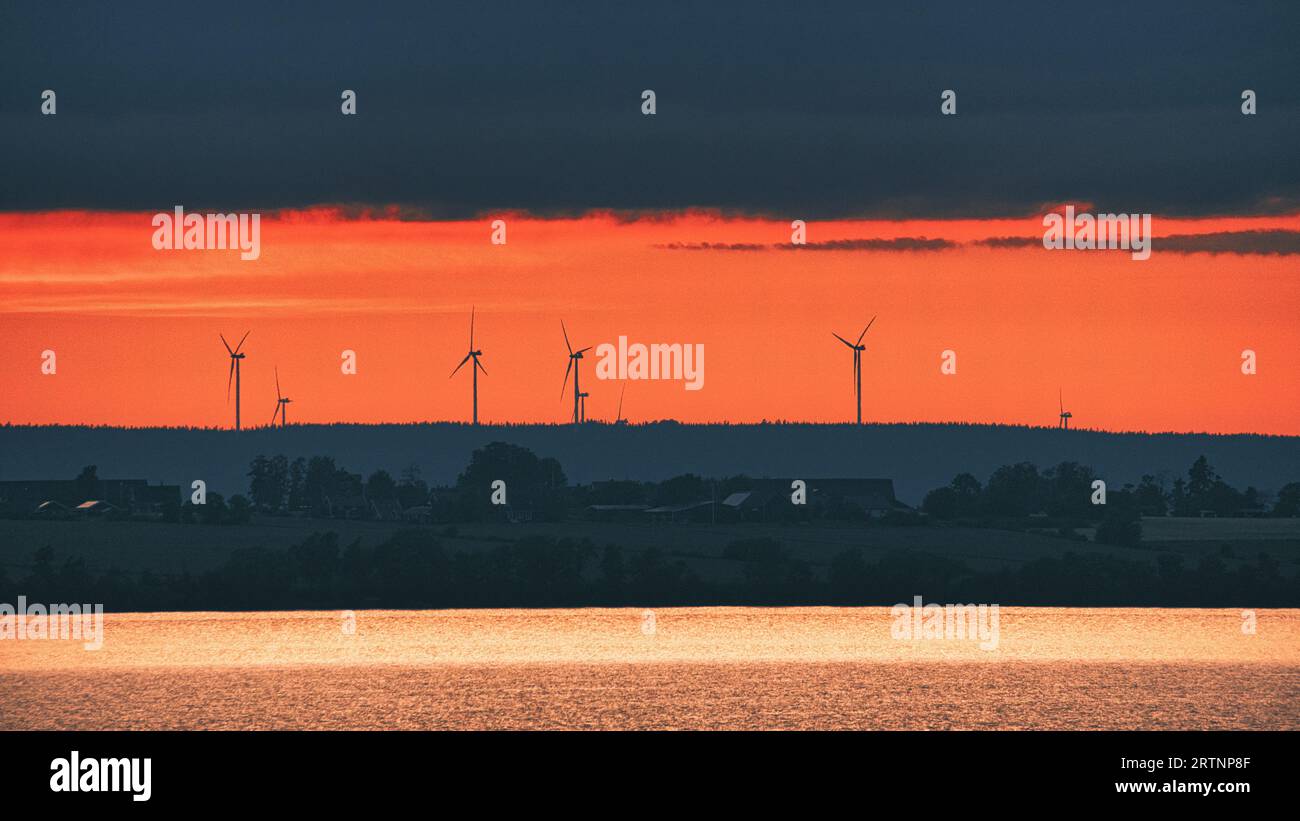 Turbina eolica, energia rinnovabile, su un lago al tramonto. Elettricità pulita per il cambiamento climatico. Cielo nuvoloso con sole arancione in Scandinavia. Foto Stock