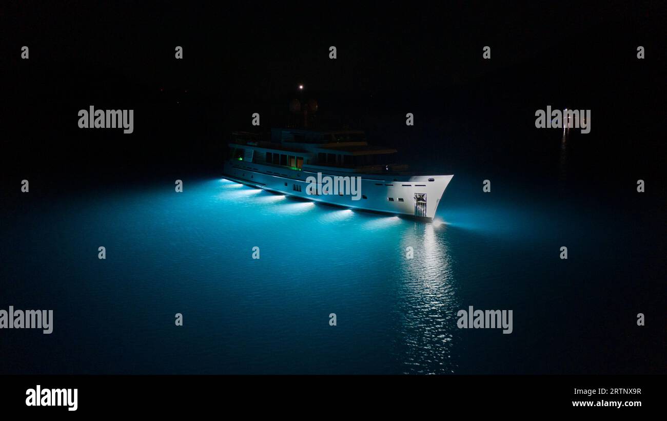 Yacht a motore di lusso, splendide luci sottomarine che illuminano le acque blu turchesi di Cavtat Bay, Croazia. Illuminazione sott'acqua Foto Stock