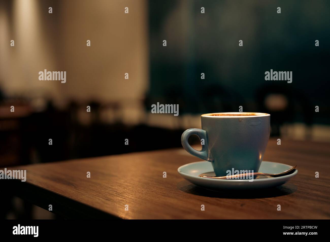 Caffè in tazza blu su un tavolo di legno nel caffè con sfondo luminoso Foto Stock