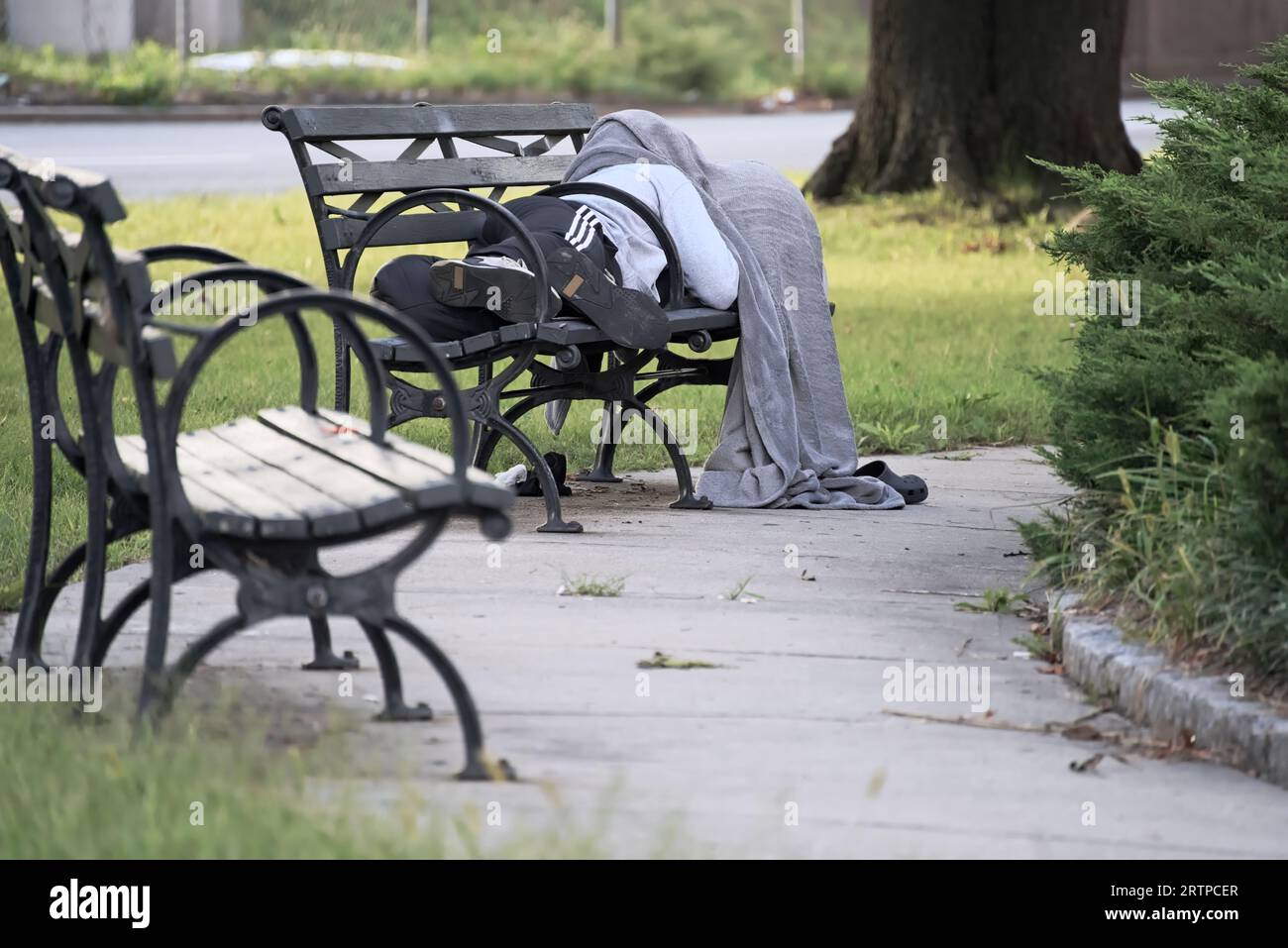 Anonimo senzatetto e possibili tossicodipendenti che dormono su una panchina del parco di New York con una coperta sopra la testa Foto Stock