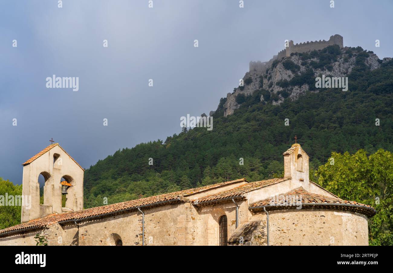 Vista panoramica dell'antica chiesa del villaggio con il castello cataro medievale di Puilaurens sulla montagna rocciosa, Aude, Francia Foto Stock