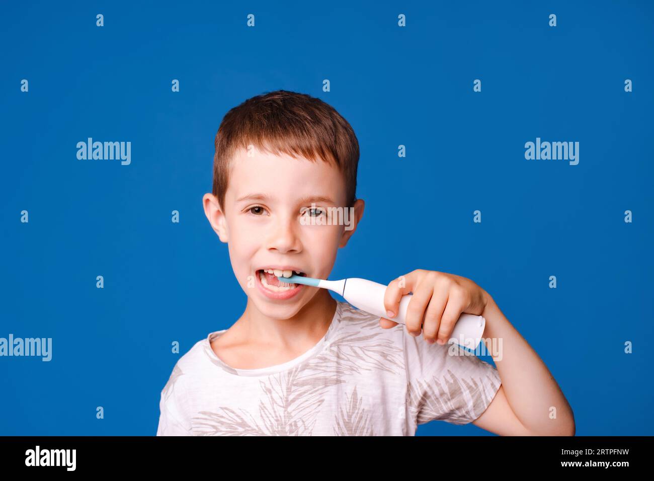 bambino spazzolino i denti con spazzolino elettrico isolato sullo sfondo blu chiaro dello studio Foto Stock