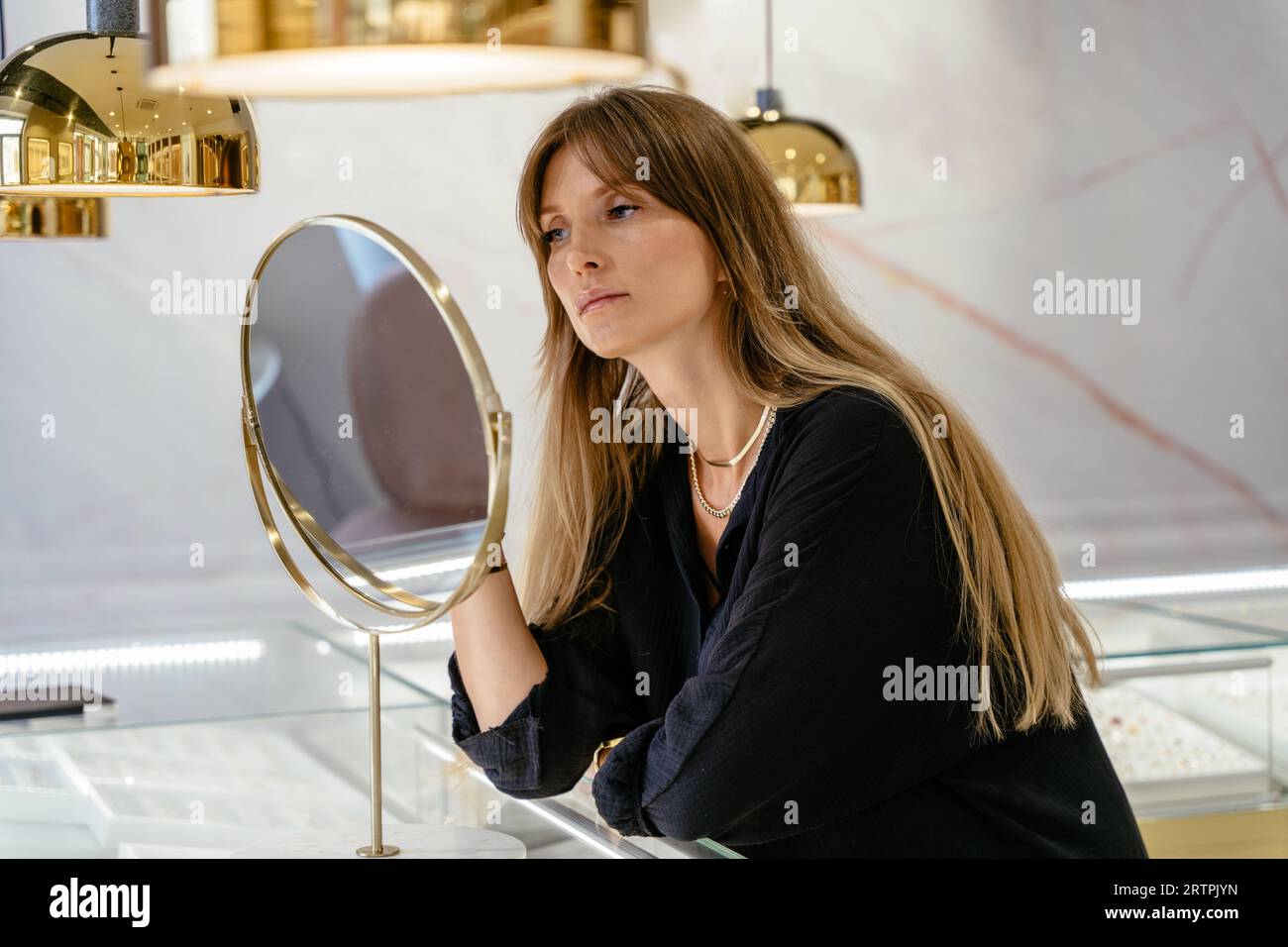 Bella donna caucasica dai capelli lunghi che sceglie gioielli in una moderna gioielleria. Foto Stock