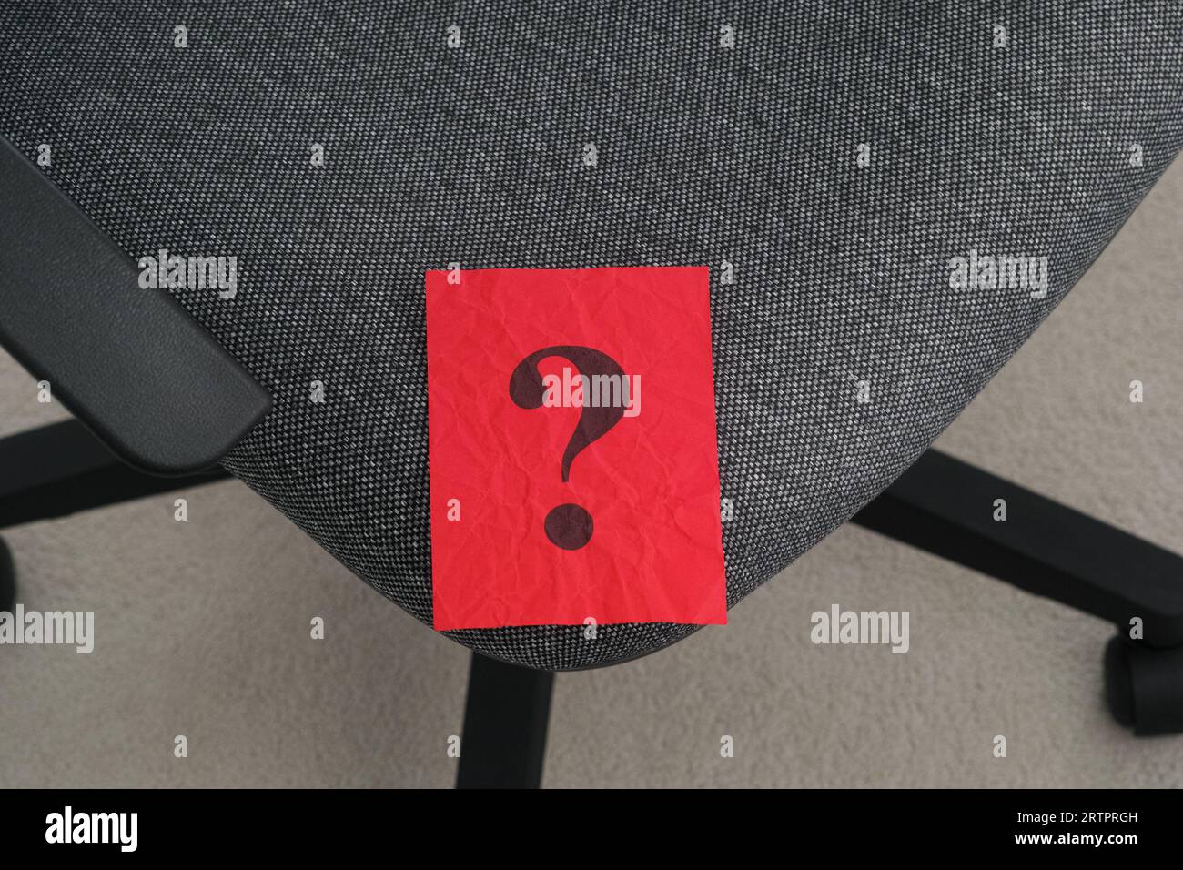 Un pezzo di carta rosso sgualcito con un punto interrogativo adagiato su una sedia da ufficio. Primo piano. Foto Stock