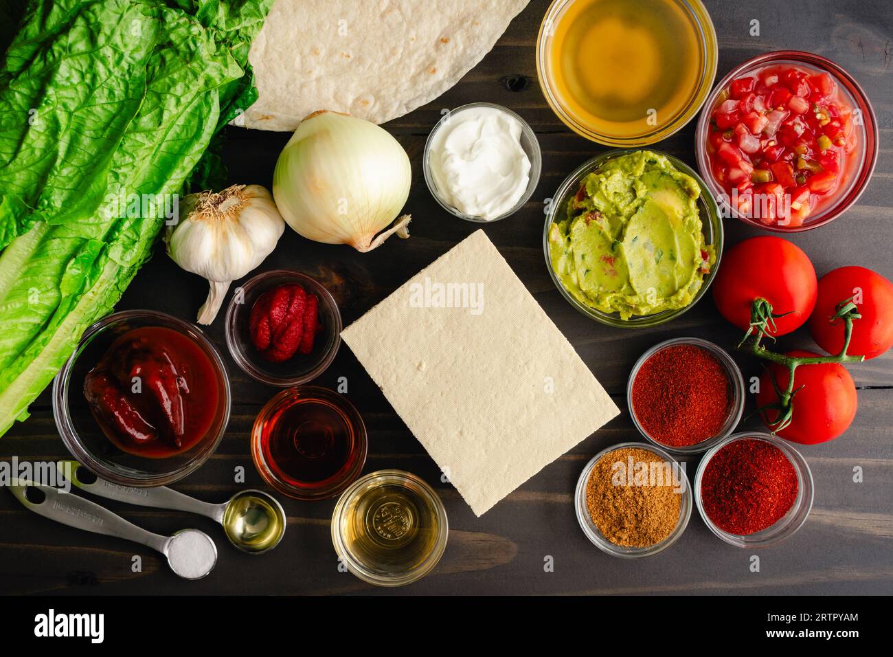 Ingredienti piccanti di tofu Burrito e condimenti su un tavolo di legno: Ingredienti e ripieni di burrito Sofritas su sfondo scuro Foto Stock