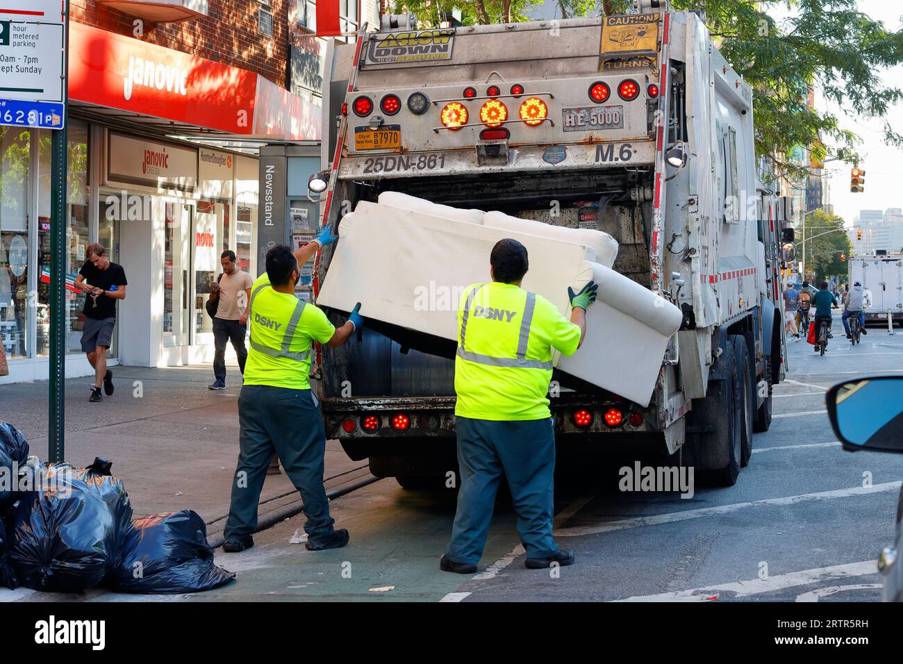 Gli operai della NYC Sanitation gettano un divano nella tramoggia di un camion della spazzatura, New York City. Foto Stock
