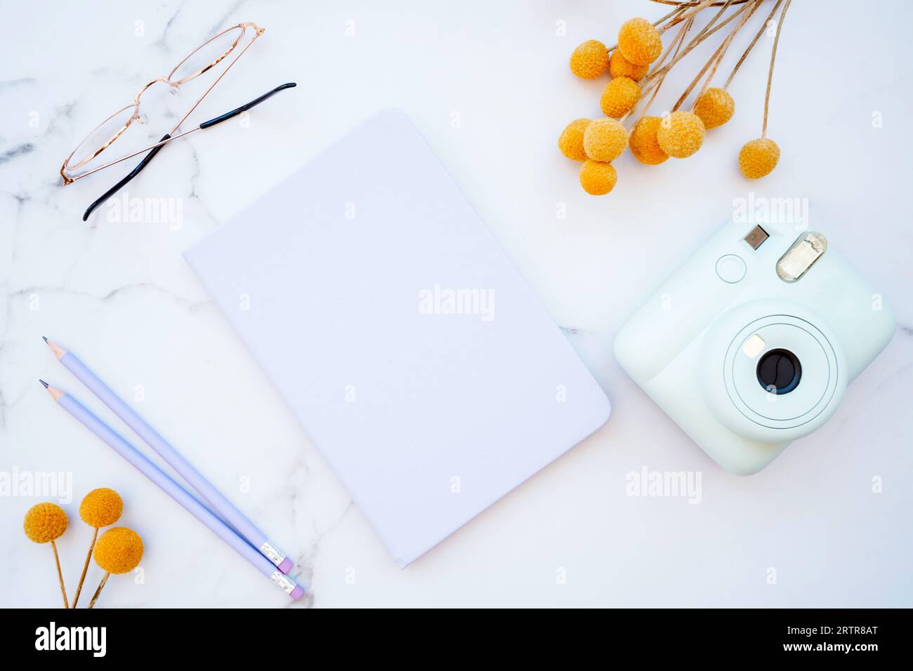 Tavolo piatto in marmo bianco con cancelleria, bicchieri, fiori gialli e macchina fotografica. Vista superiore con spazio di copia. Moderno concetto di luogo di lavoro femminile Foto Stock