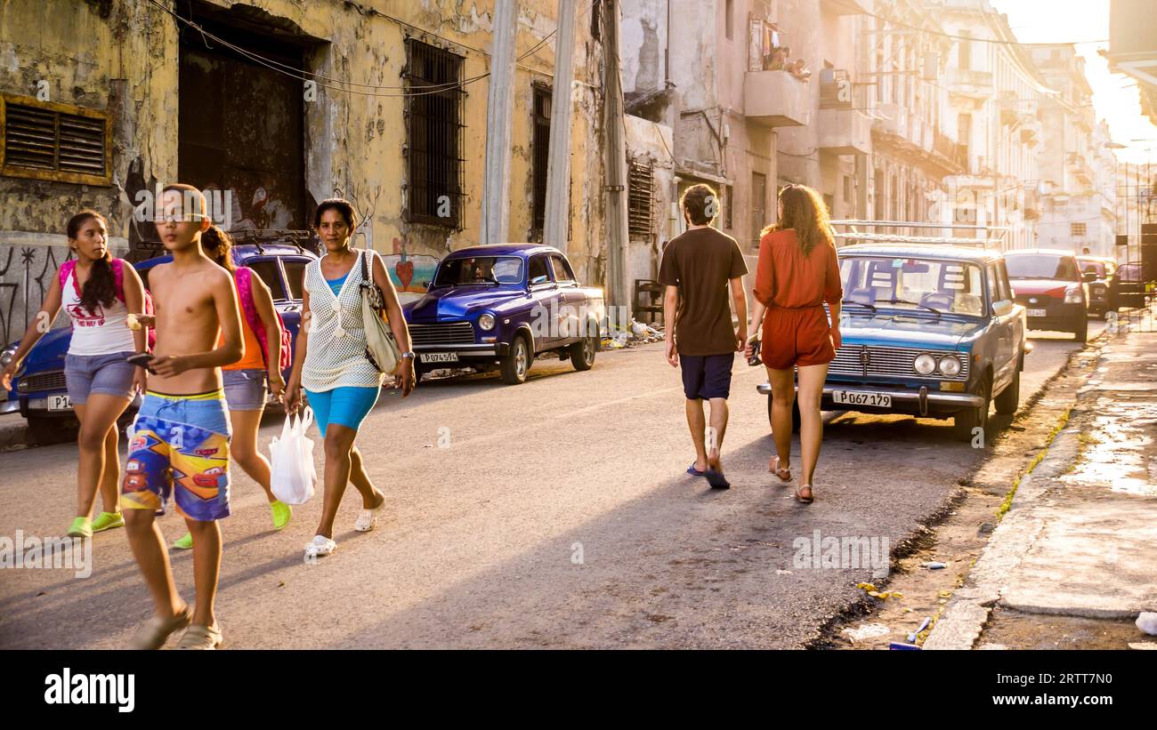 L'Avana, Cuba il 22 dicembre 2015: I cubani camminano in una strada dell'Avana vecchia al tramonto. Sul lato della strada ci sono molti oldtimer Foto Stock
