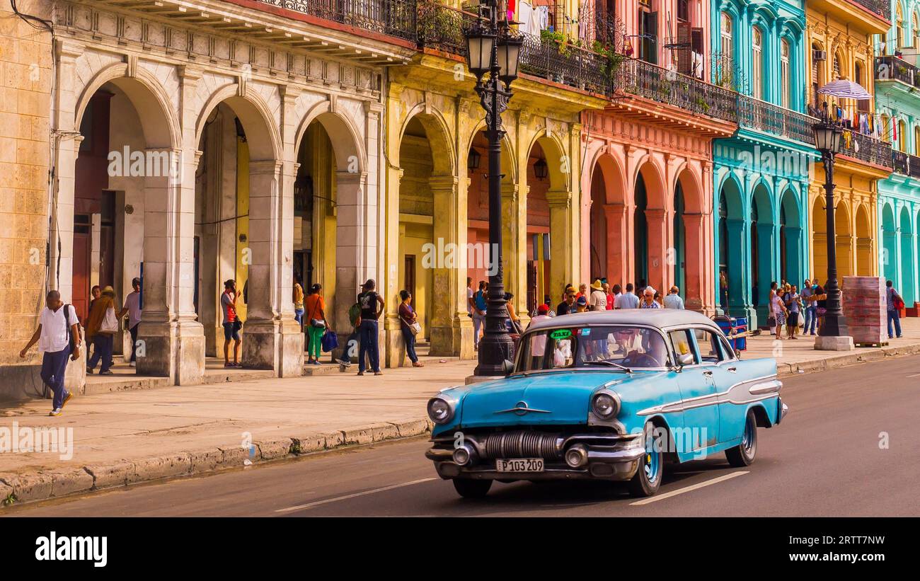L'Avana, Cuba il 22 dicembre 2015: Un taxi blu oldtimer attraversa l'Habana Vieja di fronte a una facciata colorata Foto Stock