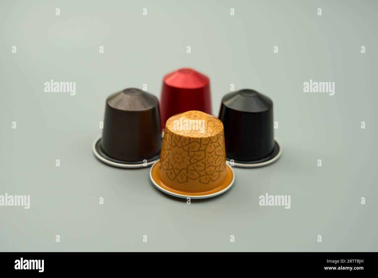 Quattro cialde di caffè in capsule di alluminio di colore rosso, marrone, nero e oro su sfondo grigio Foto Stock
