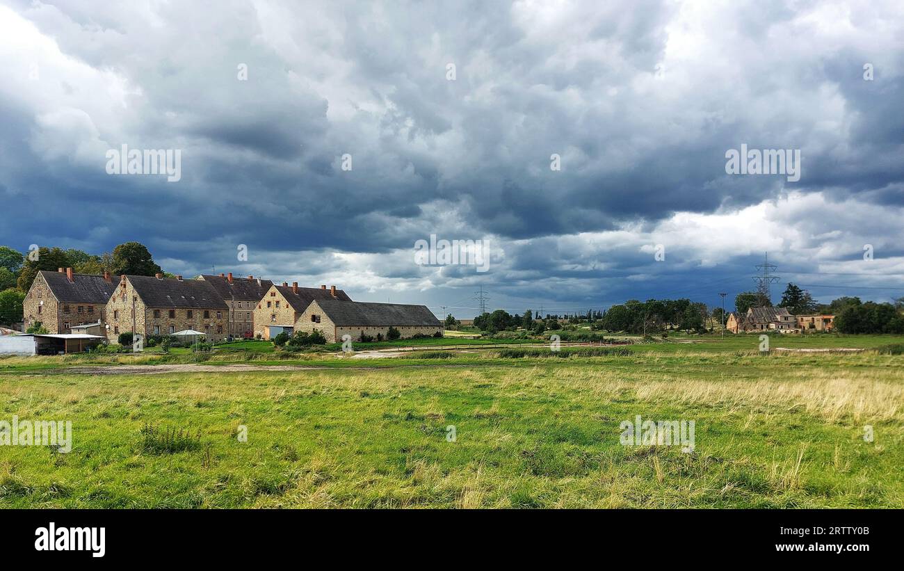 Grandi e piccoli edifici rurali sotto il cielo con nuvole di tempeste in Germania. Foto Stock