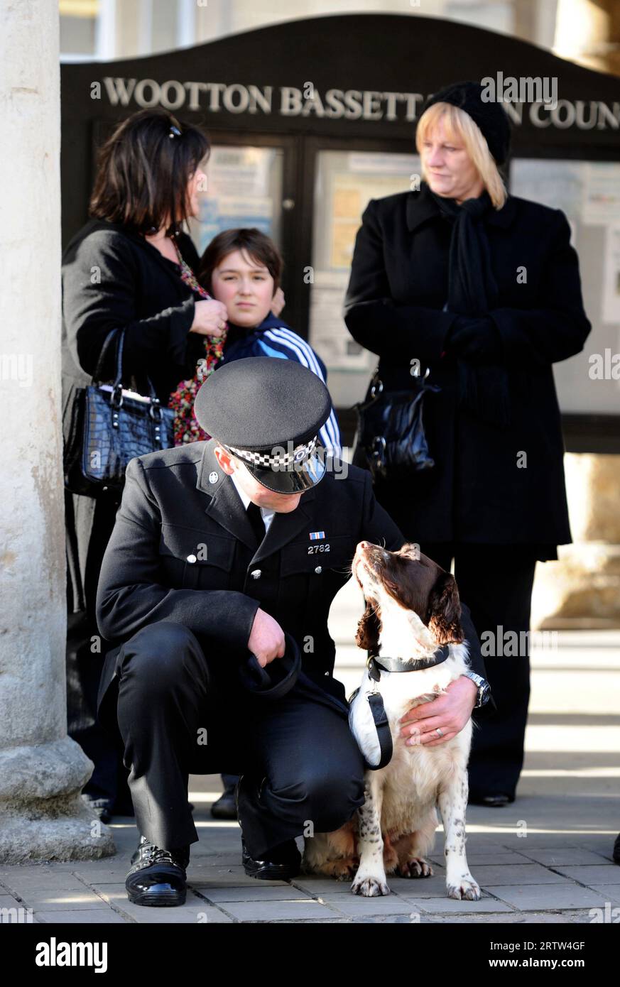 Un addestratore di cani della polizia aspetta che il corteo passi prima di una processione di rimpatrio a Wootton Bassett, Wiltshire, Regno Unito. Foto Stock