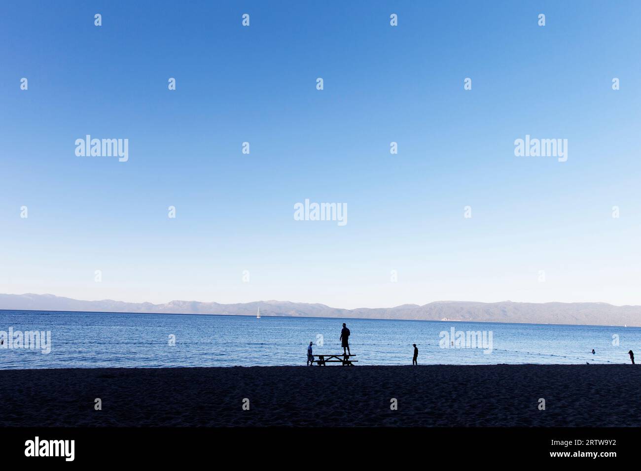 Sulla spiaggia del lago Tahoe c'è gente sagomata e retroilluminata. Foto Stock