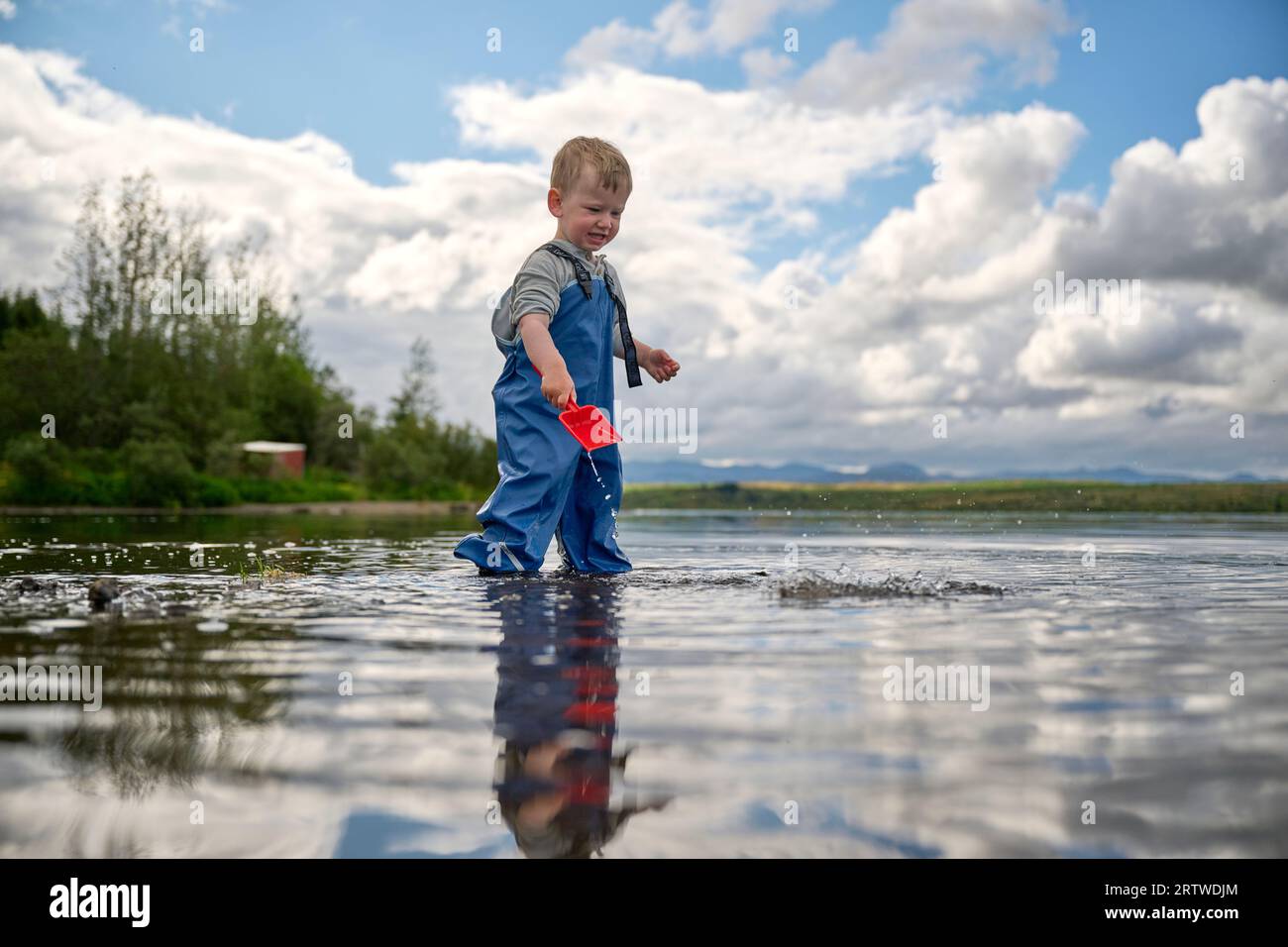 Un ragazzino carino che gioca nell'acqua del lago Foto Stock