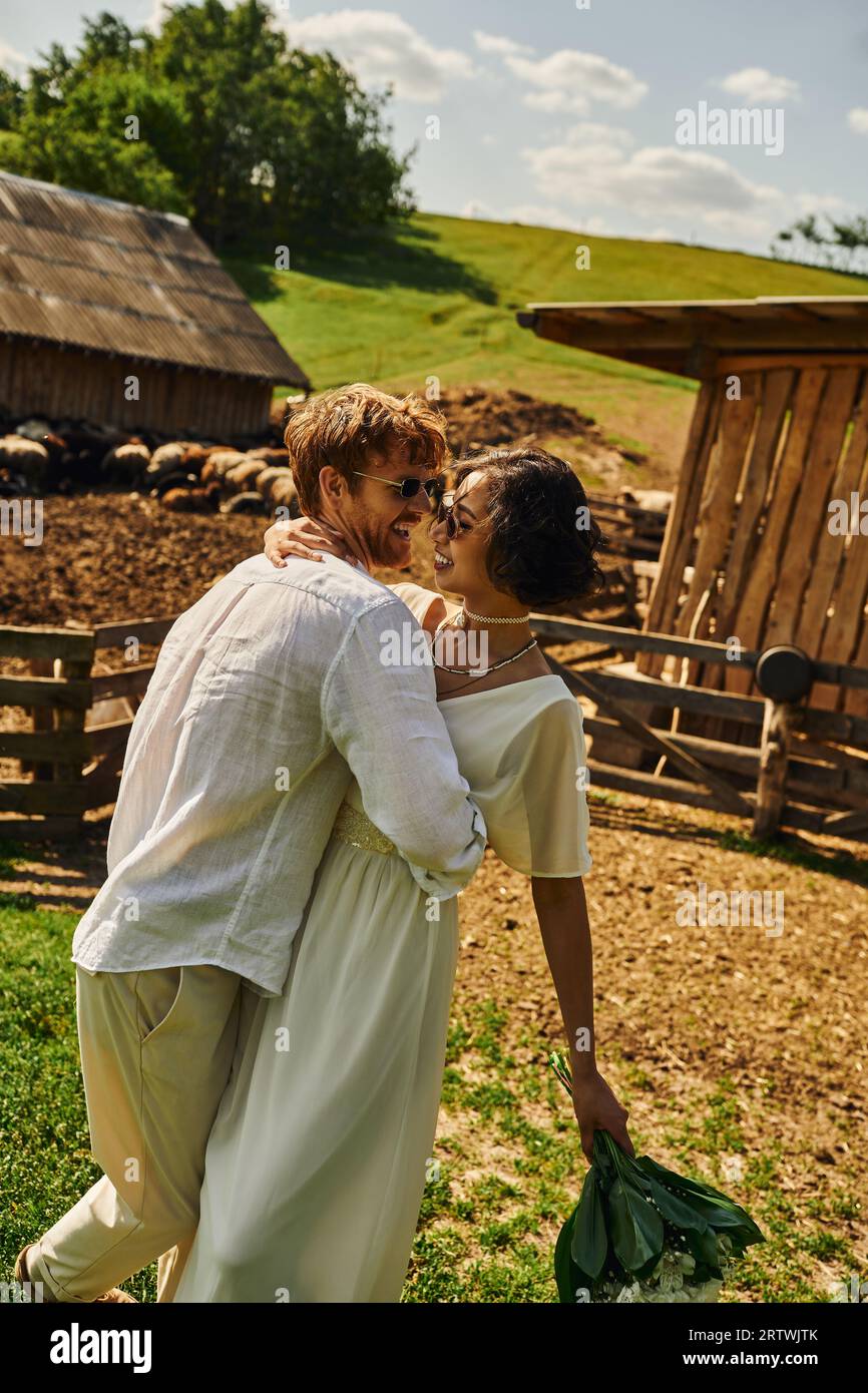 matrimonio rustico in stile boho, sposa asiatica interrazziale che abbraccia lo sposo vicino al bestiame in fattoria Foto Stock matrimonio rustico in stile boho, sposa asiatica interrazziale che abbraccia lo sposo vicino al bestiame in fattoria Foto Stock