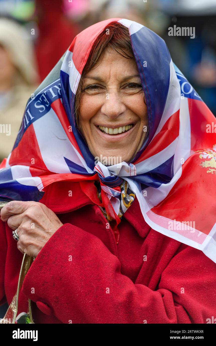 Una donna che indossa una bandiera Union Jack come un velo fa parte di una grande folla che sfiora la pioggia per guardare l'incoronazione di re Carlo III, su una TV gigante Foto Stock