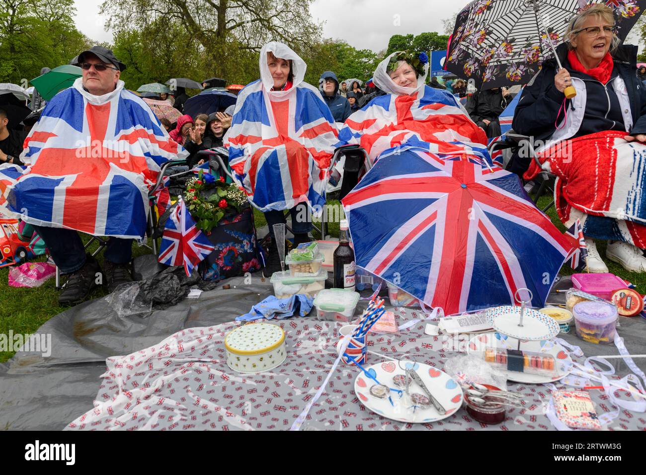 Un gruppo sedeva con il loro picnic sotto la pioggia, mentre guardavano l'incoronazione di re Carlo III, su un gigantesco schermo televisivo. Fanno parte di una grande folla di brav Foto Stock Un gruppo sedeva con il loro picnic sotto la pioggia, mentre guardavano l'incoronazione di re Carlo III, su un gigantesco schermo televisivo. Fanno parte di una grande folla di brav Foto Stock