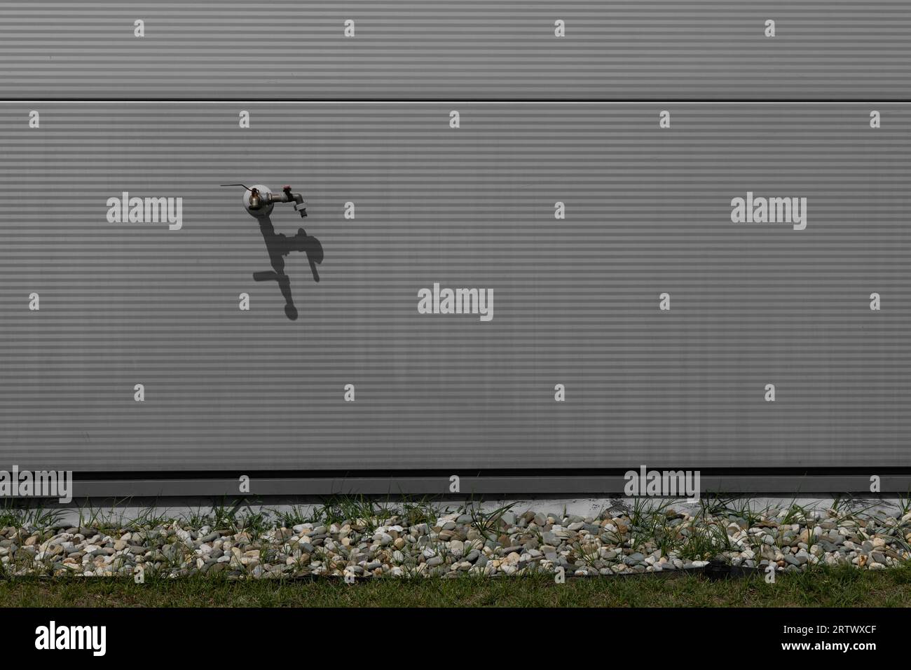 Rubinetto dell'acqua per innaffiare il prato su una parete grigia Foto Stock