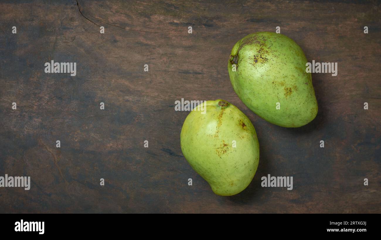 due mango su un tavolo rustico in legno, mangifera indica, popolare frutto tropicale originario dell'asia meridionale e conosciuto per il suo delizioso dolce e succoso Foto Stock