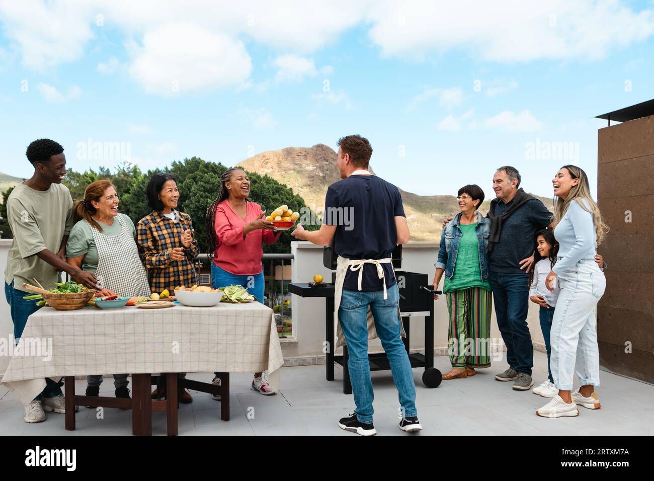 Amici multigenerazionali che si divertono a fare barbecue sul tetto della casa - felici persone multirazziali che cucinano insieme Foto Stock