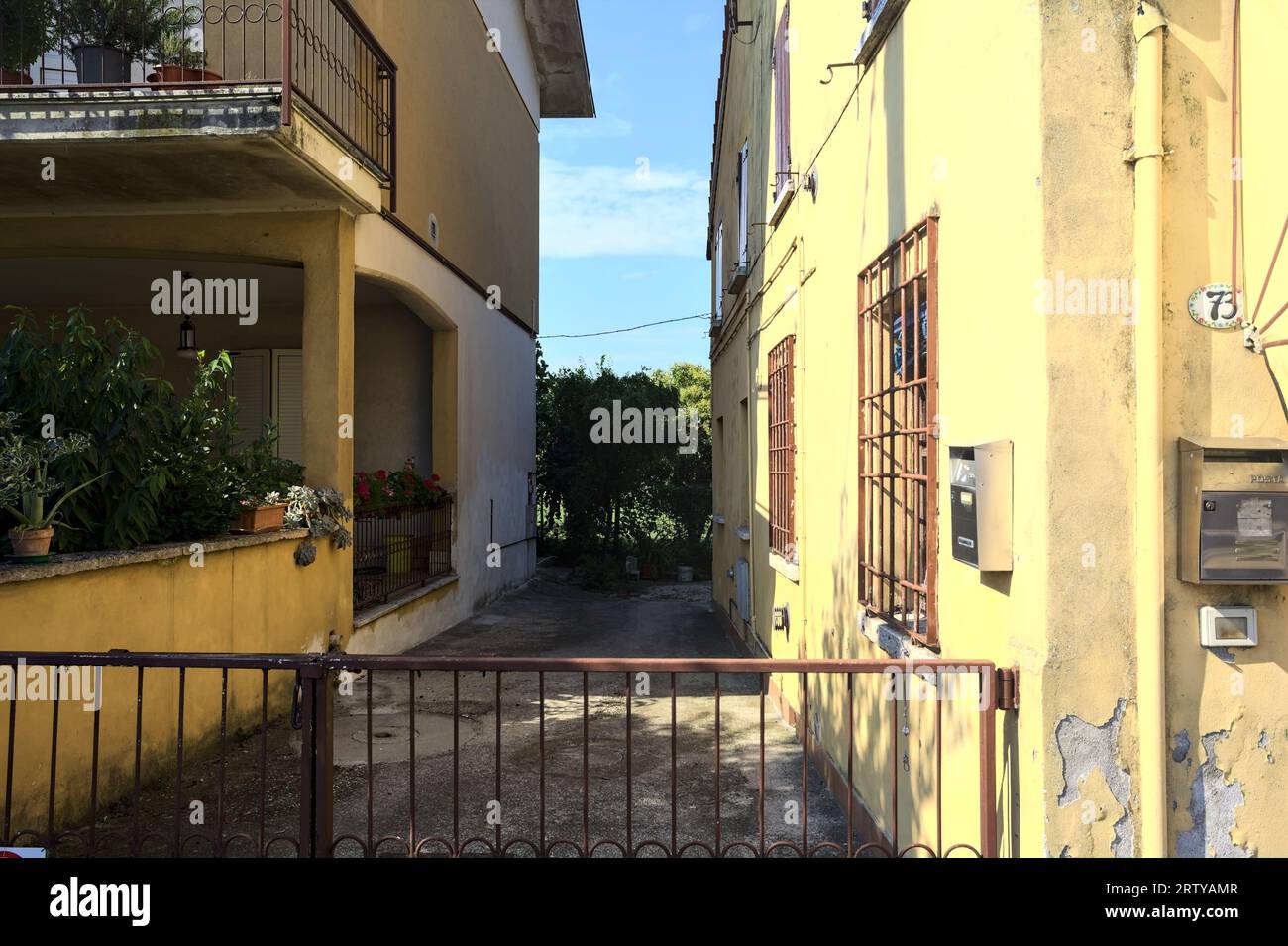 Sentiero d'ingresso tra due case in un villaggio italiano in campagna di giorno bloccato da un cancello Foto Stock