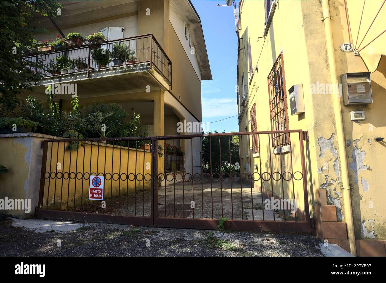 Sentiero d'ingresso tra due case in un villaggio italiano in campagna di giorno bloccato da un cancello Foto Stock