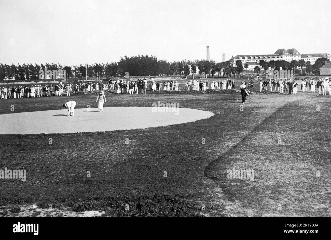 Palm Beach, Florida c. 1921 la galleria di golf che guarda una donna giocatrice che mette sulla 13a buca. Il Breakers Hotel è sullo sfondo. Foto Stock