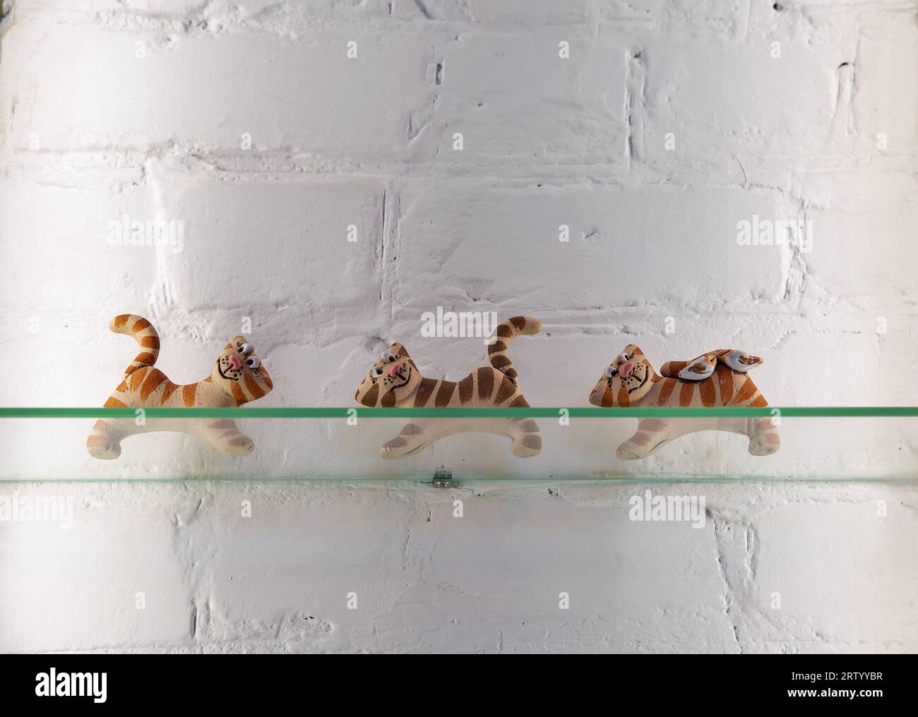 primi piani decorativi di graziose tigri su uno scaffale di vetro contro una parete di mattoni bianchi Foto Stock