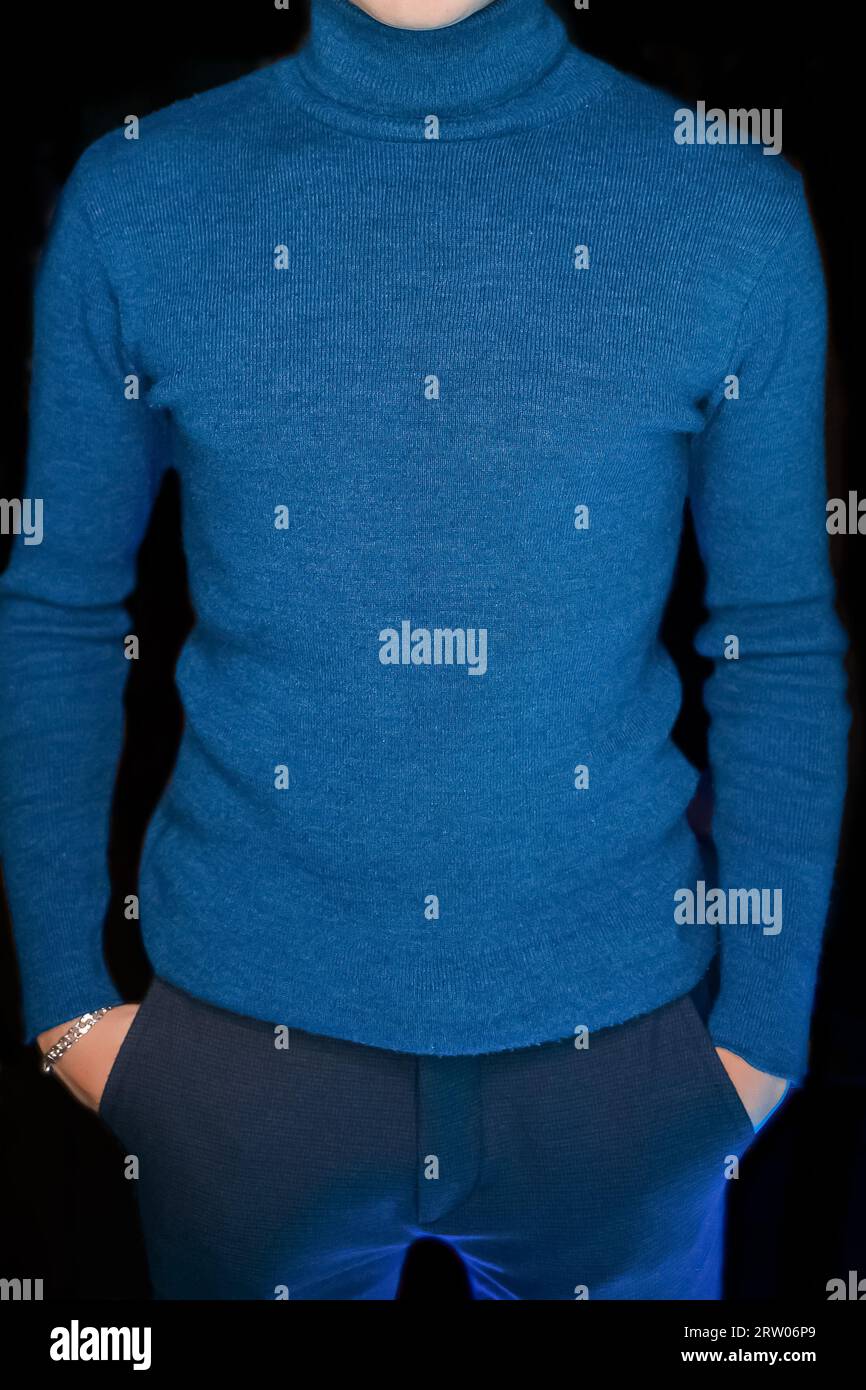 Uomo magro in stile blu dolcevita con le mani in tasca in posa su sfondo nero. Foto Stock