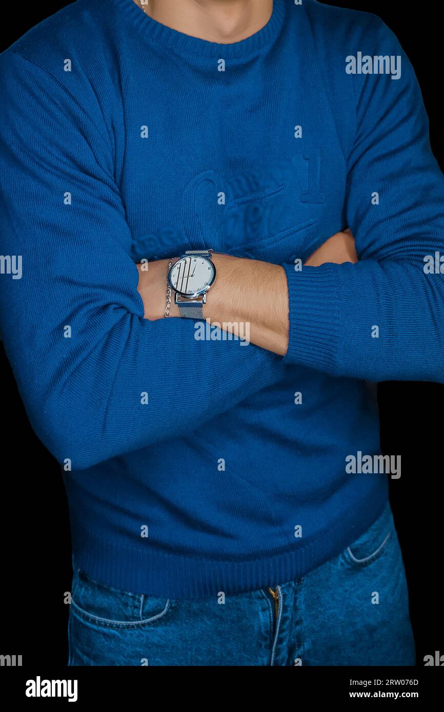 Uomo in posa con un orologio da polso in maglione blu, moda e stile di abbigliamento su sfondo scuro. Foto Stock