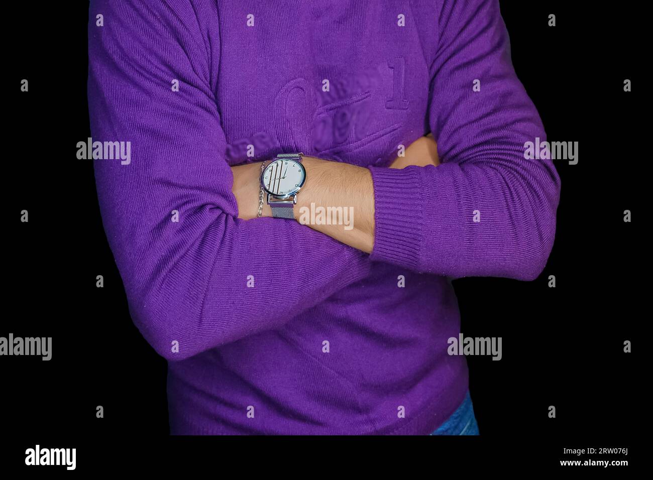 Uomo in posa con un orologio da polso in maglione viola, stile e stile di abbigliamento su sfondo nero scuro. Foto Stock