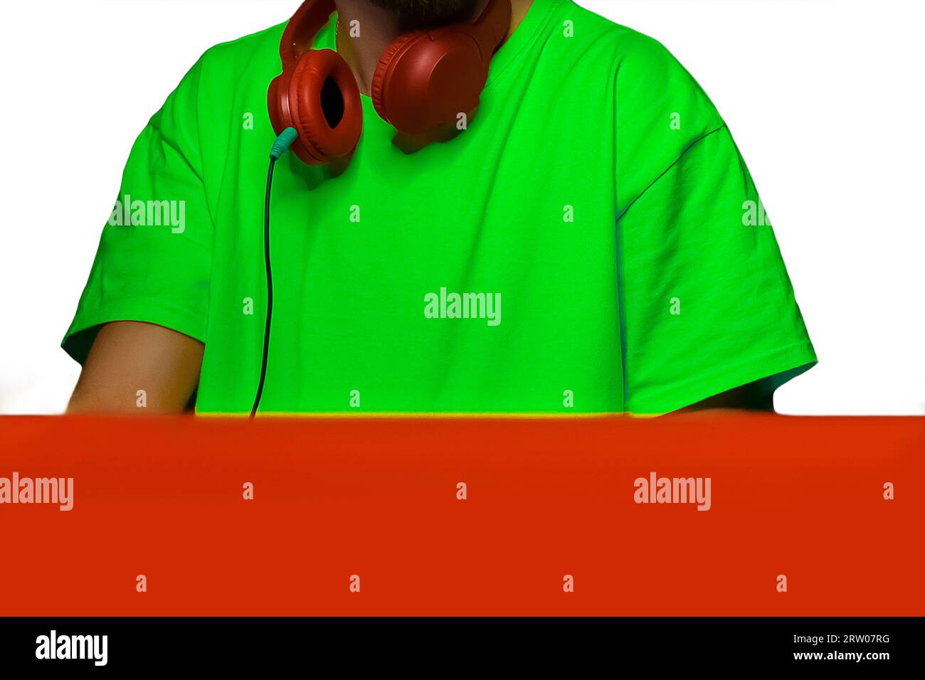 DJ elegante e alla moda con cuffie rosse intorno al collo in una camicia oversize a tema club color verde chiaro su uno sfondo bianco isolato. Foto Stock